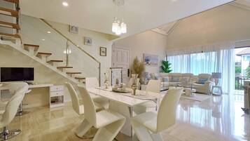 Un amplio espacio habitable con una mesa de comedor, sillas blancas, un sofá y una escalera.