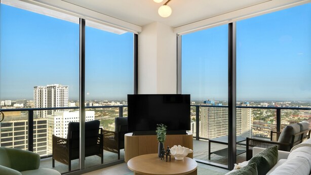 A modern living room with a large TV, comfortable seating, and a balcony with a city view. - Crosby Miami WTC 2BR/2BA Top Floor Residence #3214 (Miami)