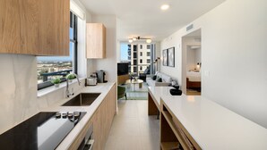 A modern kitchen with a stove, sink, and window overlooking a cityscape. - Crosby Miami WTC 2BR/2BA Top Floor Residence #3214 (Miami)