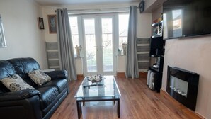 Un salón con un sofá de cuero negro, una mesa de centro de vidrio, una chimenea y un televisor.