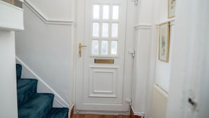 Una puerta blanca con manija de bronce, una ventana de múltiples cristales y una escalera con alfombra azul.