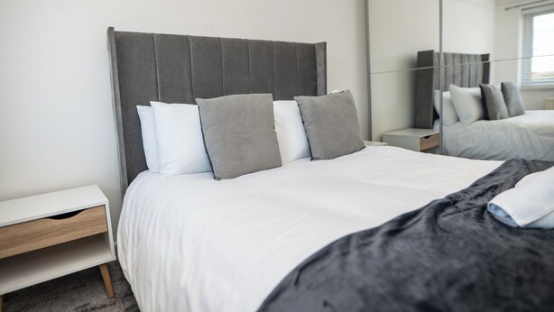 Un dormitorio moderno con cama, mesitas de noche y un espejo grande.