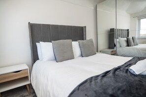Un dormitorio moderno con cama, mesitas de noche y un espejo grande.