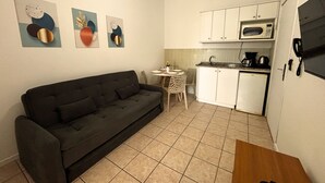 Ett kompakt bostadsutrymme med en soffa, ett litet matbord, en liten köksdel med mikrovågsugn och en kaffebryggare.