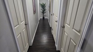 A hallway with white doors, dark wooden flooring, and a plant in the center.