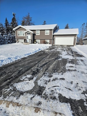 Ein Wohnhof mit Schnee, eine Garage und ein Haus mit brauner Fassade und weißen Verzierungen.