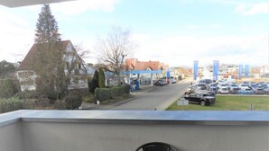 Un balcon avec une table et des chaises, donnant sur un parking où se trouvent des voitures, avec un bâtiment en arrière-plan.