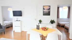 Un salon moderne avec un coin repas, un téléviseur à écran plat fixé au mur, une petite table avec un panier de fruits et un canapé à l’arrière-plan.