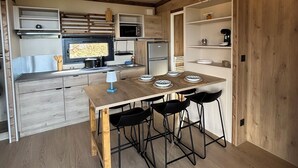Una cocina moderna con vigas de madera, una isla central con taburetes, electrodomésticos integrados y una lámpara colgante.