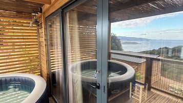 Une terrasse en bois avec un jacuzzi et une porte vitrée donnant sur un paysage magnifique.