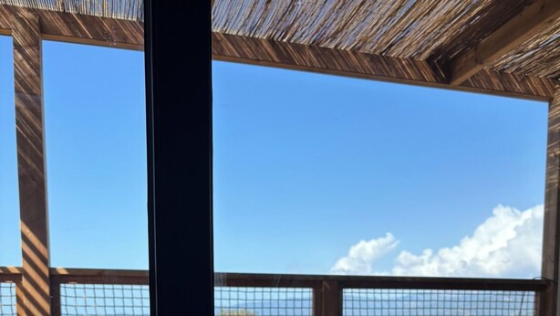 Una habitación con cama, vista a través de una ventana de malla y techo de madera.