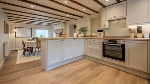 A kitchen with wooden beams, white cabinets, a dining area with a table and chairs, and an oven. - Charming Countryside Cottage Yorkshire Dales (Richmond)