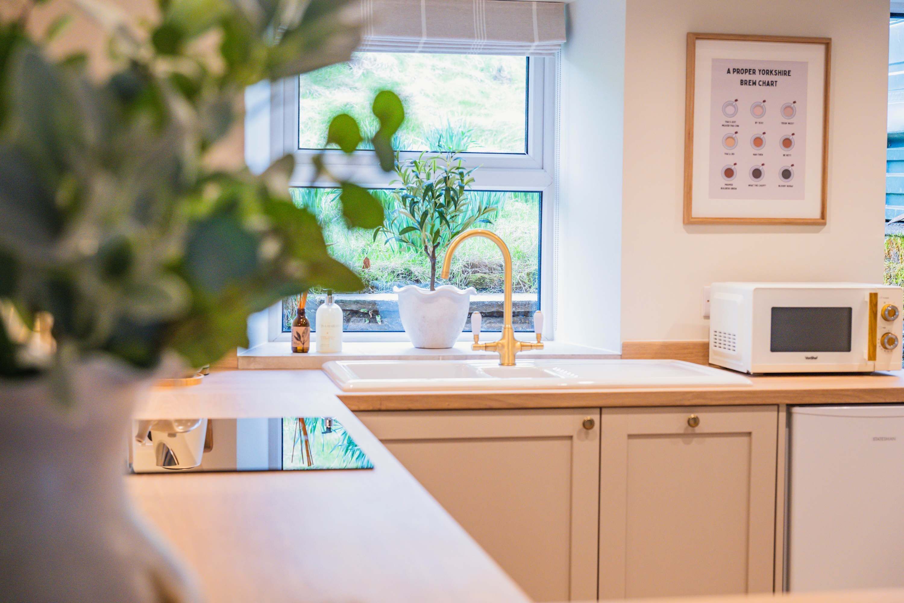 A kitchen with a sink, a white microwave, and a framed brew chart on the wall.