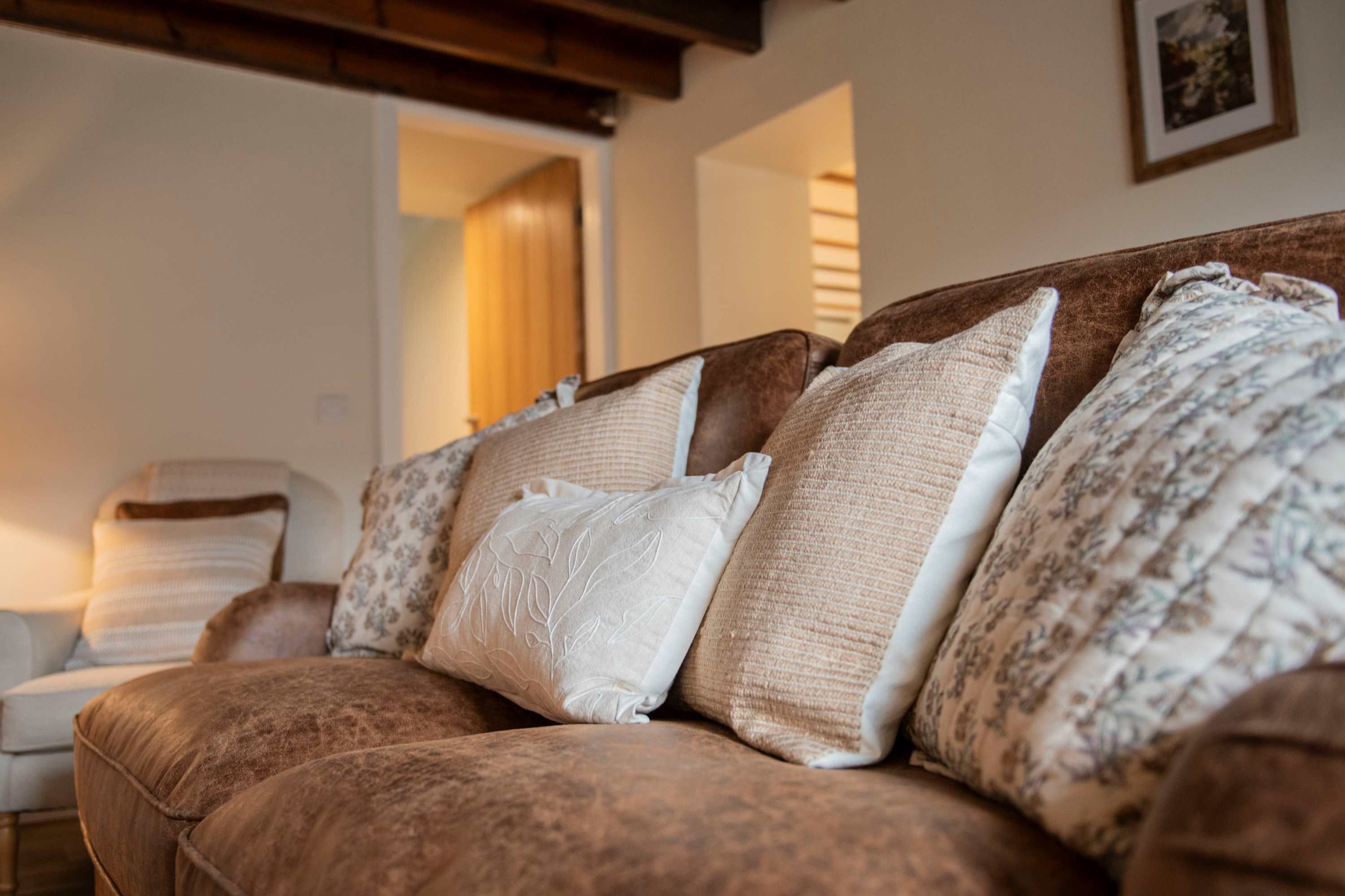 Un canapé marron avec des coussins à motifs, dans une pièce dont le plafond est en bois et où un tableau encadré est accroché au mur.