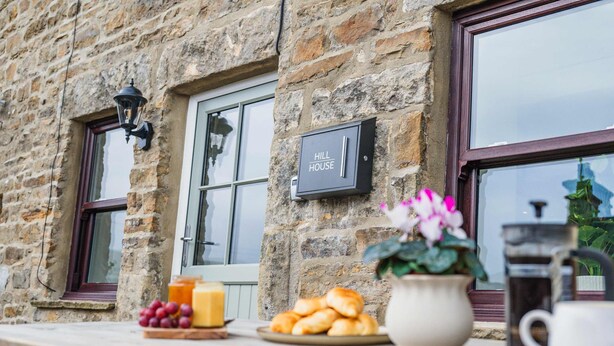 A stone building with a sign reading 'HILL HOUSE,' a window with a view, and a table with food and drinks. - Charming Countryside Cottage Yorkshire Dales (Richmond)