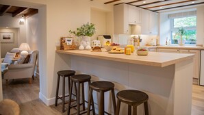 A modern kitchen with a central island, bar stools, and a dining area with a sofa and lamp. - Charming Countryside Cottage Yorkshire Dales (Richmond)