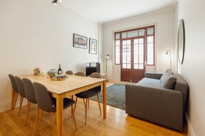 A modern living room with a wooden dining table, grey sofa, and a large window with a view. - City Center Terrace Apartment by Vacationy (Porto)