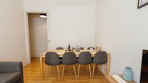Ruokailutilassa on puinen pöytä, neljä tuolia, sohva, televisio ja maljakko.