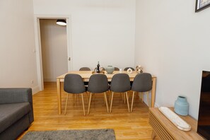 Un comedor con una mesa de madera, cuatro sillas, un sofá, un televisor y un florero.