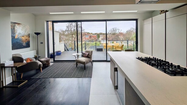 Eine moderne Küche mit großem Fenster, ein Essbereich mit Tisch und Stühlen sowie ein Wohnbereich mit Sofa und einem Gemälde.