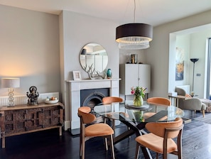 Ein modernes Wohnzimmer mit Kamin, einem runden Spiegel, einer Chandelier-Leuchte und einem Esstisch mit Glasplatte und orangefarbenen Stühlen.