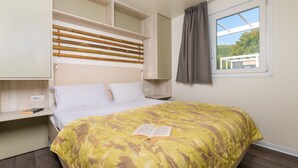 A bedroom with a bed, a bedside table, a built-in shelf, a window with a view, and a curtain. - Mobile Home in Rabac With Shared Pool (Labin)
