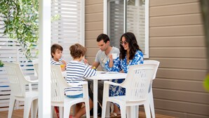 A family dining outdoors at a white table with a beige house in the background. - Mobile Home in Rabac With Shared Pool (Labin)