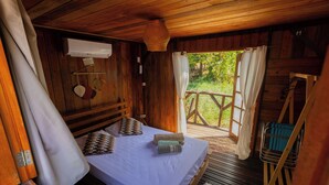 A wooden cabin with a bed, a hanging light fixture, and a view of the outdoors.