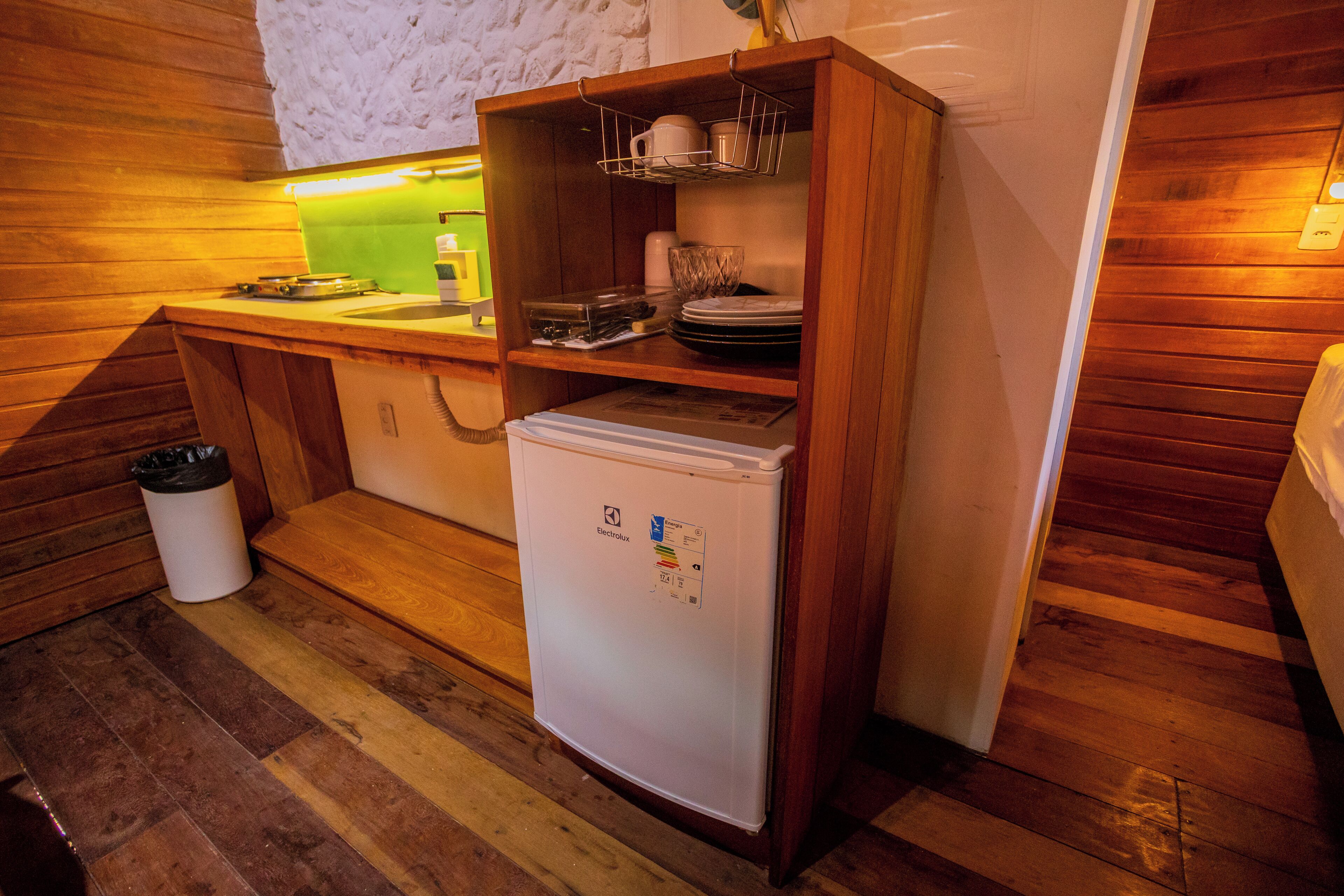 A compact kitchen with a refrigerator, wooden cabinets, a sink, and a trash bin.