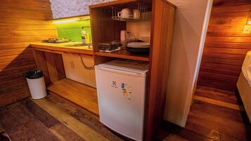 A compact kitchen with a refrigerator, wooden cabinets, a sink, and a trash bin.
