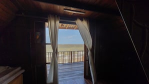 A wooden deck with a view of the sea, curtains on the windows, and a ceiling light fixture.