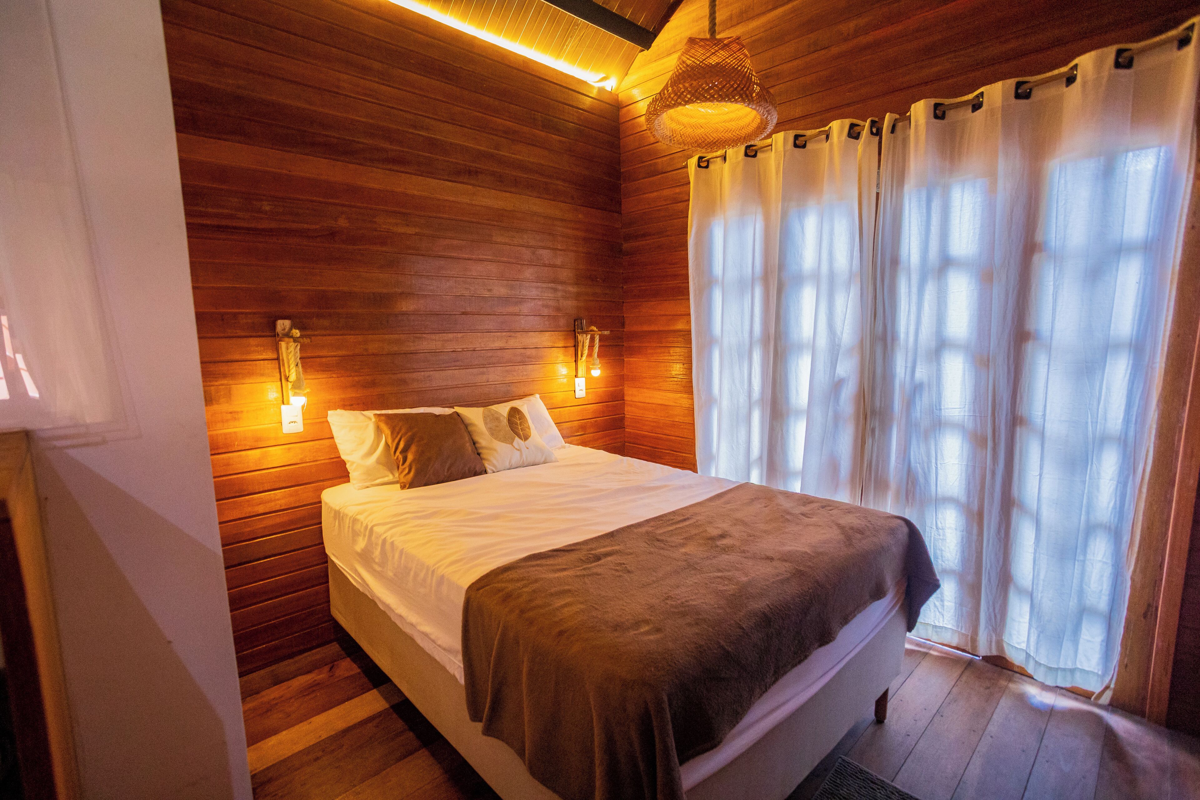 A wooden-paneled room with a bed, wall-mounted lights, and a window with curtains.