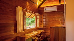 A wooden cabin interior with a bench, a table, a window with curtains, and an air conditioning unit.
