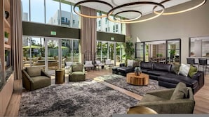 Eine großzügige Lobby mit einer großen schwarzen Ledersofa, mehreren Sesseln, einem Couchtisch und einem großen Fenster mit Blick ins Freie.