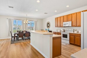 A modern kitchen with wooden cabinets, a central island, and a dining area with a chandelier. - Spacious 6BR home w/ pool & BBQ grill (Kissimmee)
