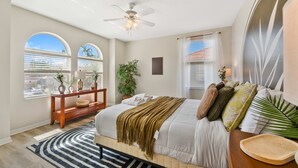 Ein Schlafzimmer mit Bett, Deckenventilator, Fenster mit Jalousien, Nachttisch und Beistelltisch.