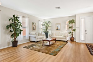 A living room with two white sofas, a wooden coffee table, and large potted plants. - Spacious 6BR home w/ pool & BBQ grill (Kissimmee)