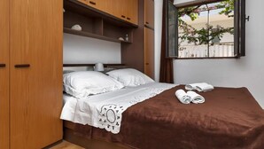 Een slaapkamer met een bed, een houten garderobe en een raam met uitzicht op bomen en een hek.