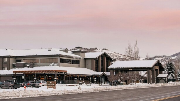 A hotel with a covered outdoor seating area, a sign indicating it is a Peaks Hotel, and a snow-covered landscape in the background. - Park City Peaks (Park City)