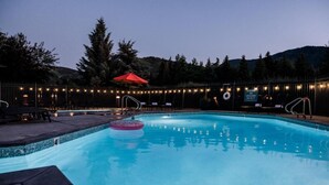 A swimming pool with a lifeguard on duty sign, surrounded by trees and a fence with string lights. - Park City Peaks (Park City)