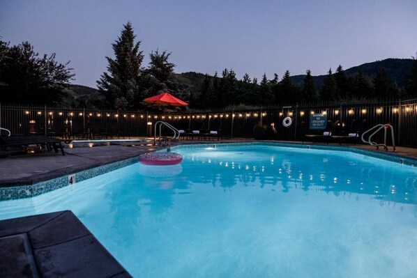 A swimming pool with a lifeguard on duty sign, surrounded by trees and a fence with string lights. - Park City Peaks (Park City)