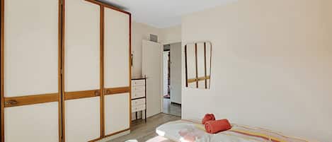 A bedroom with a bed, a wardrobe, a mirror, and a door leading to another room.