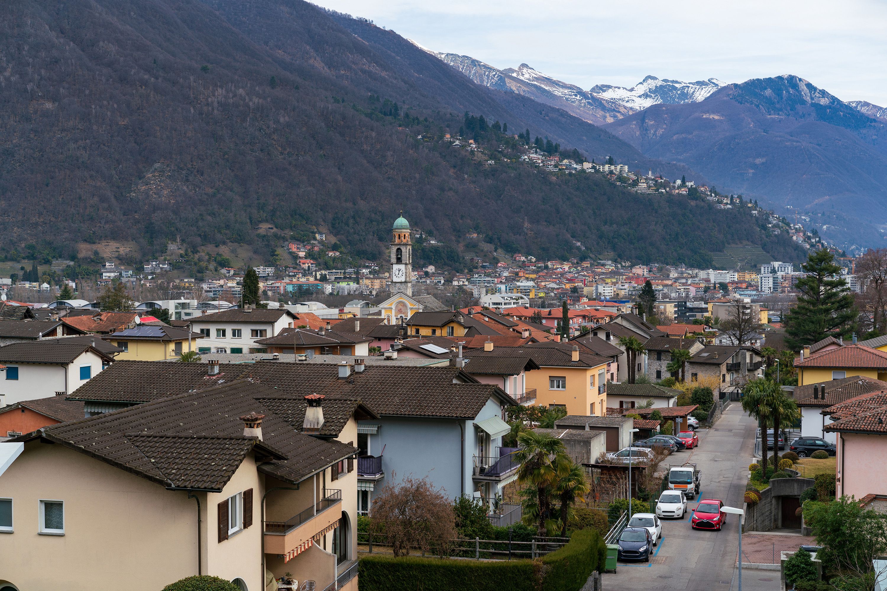 Une ville qui se distingue par son imposant clocher, entourée de bâtiments résidentiels et dominée par un paysage montagneux.