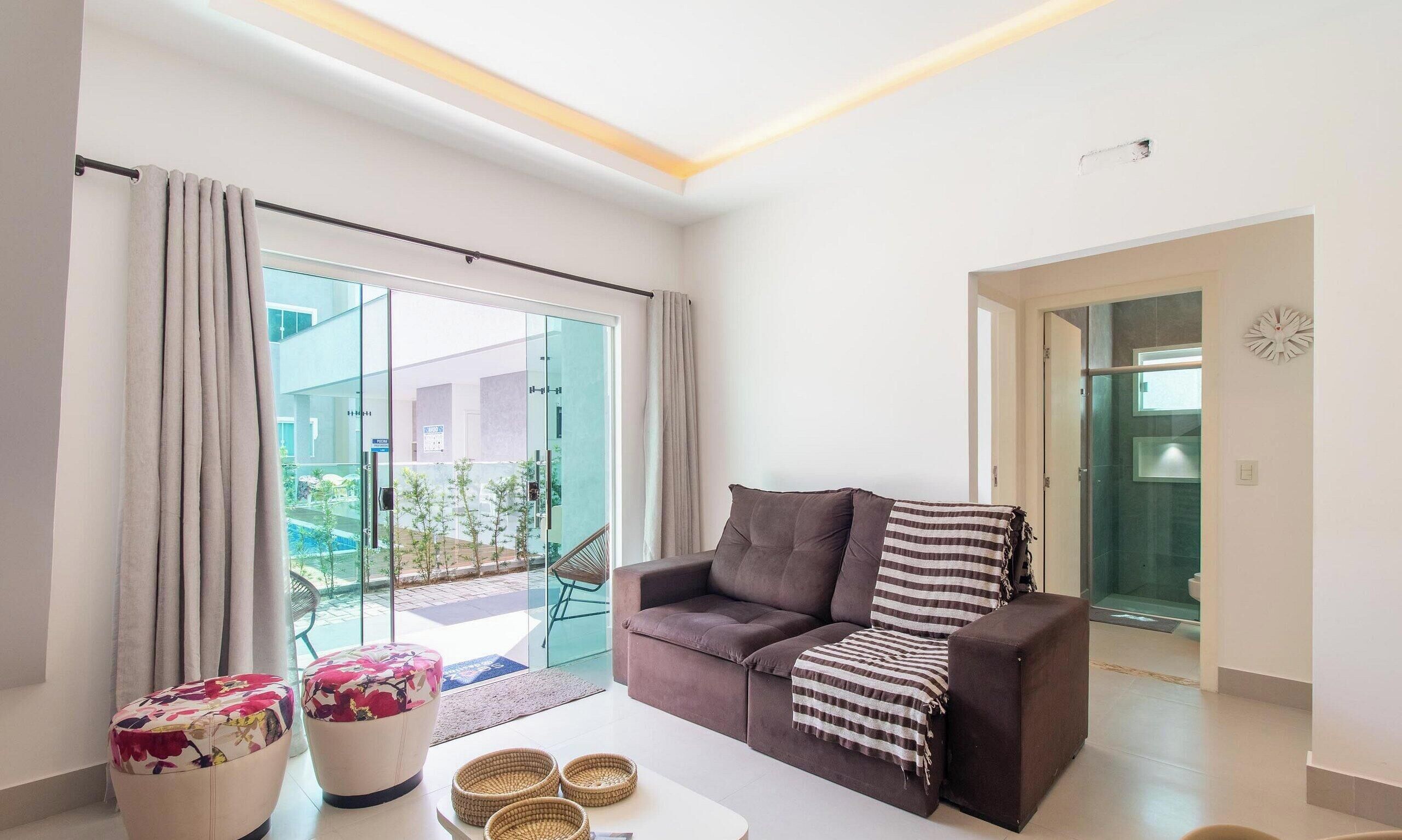 A modern living room with a sofa, ottoman, and a glass door leading to an outdoor area.