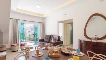 A modern living room with a dining table set, a sofa, a large mirror, and a view through a glass door.