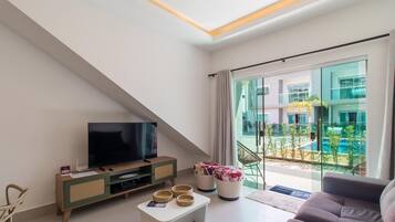 A modern living room with a flat-screen TV, a sofa, a coffee table, and a balcony with a pool view.