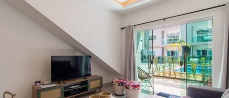 Una sala de estar moderna con un televisor de pantalla plana, un sofá, una mesa de centro y un balcón con vistas a la piscina.