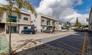 A modern building with a parking lot, multiple cars, and palm trees. - Apts in Condominium w/ Pool 450 Meters fr/ Taperapuan Beach - Atas (Porto Seguro)