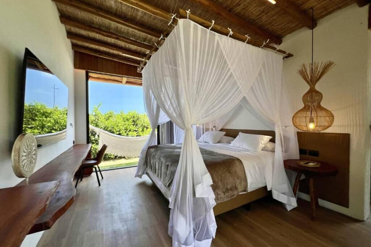 Un dormitorio con cama a dosel, una hamaca, un banco de madera y un ventanal con vistas.