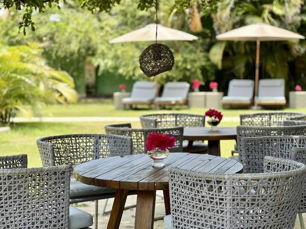 Outdoor wicker furniture, round tables, and umbrellas in a garden setting.